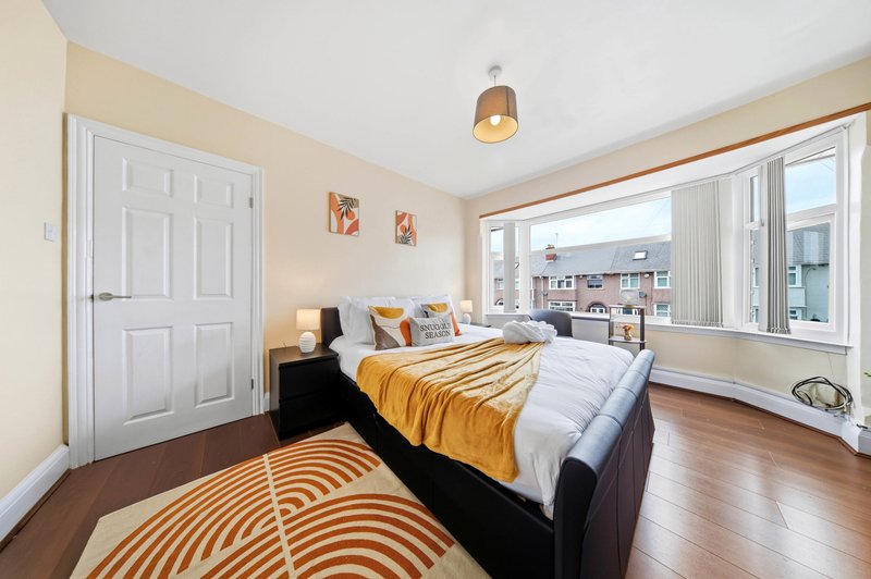 Bright bedroom with double bed, yellow bedding, wooden floor, and large windows overlooking cityscape