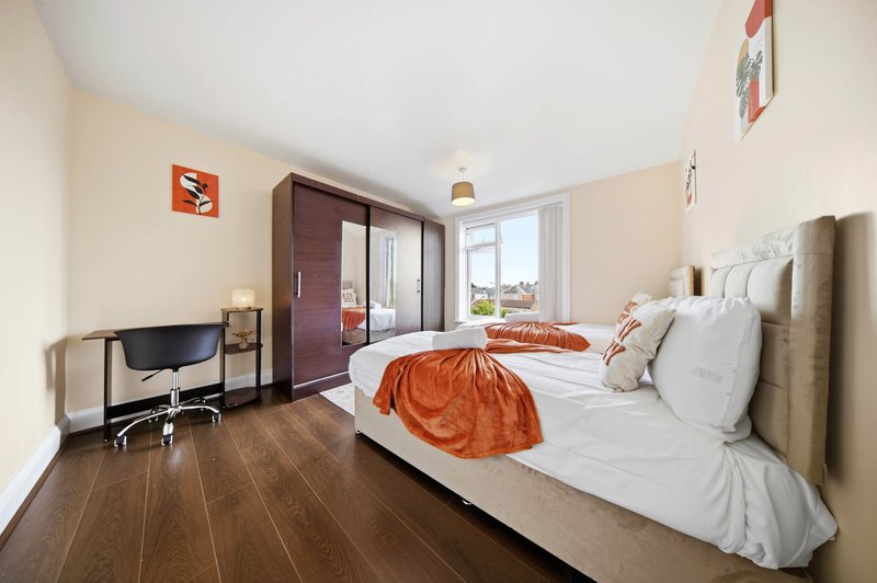 Bright bedroom with double bed, orange throw, wooden flooring, desk area and large window
