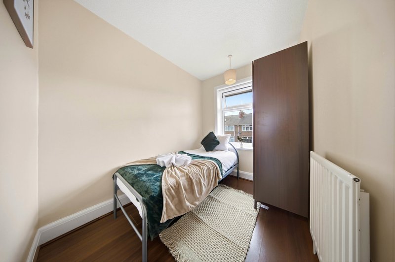 Small bedroom with single bed, wooden wardrobe, window view and radiator