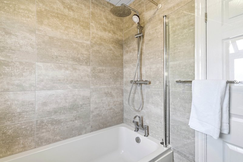 Modern bathroom with bathtub, glass shower screen, beige tile walls and towel rail