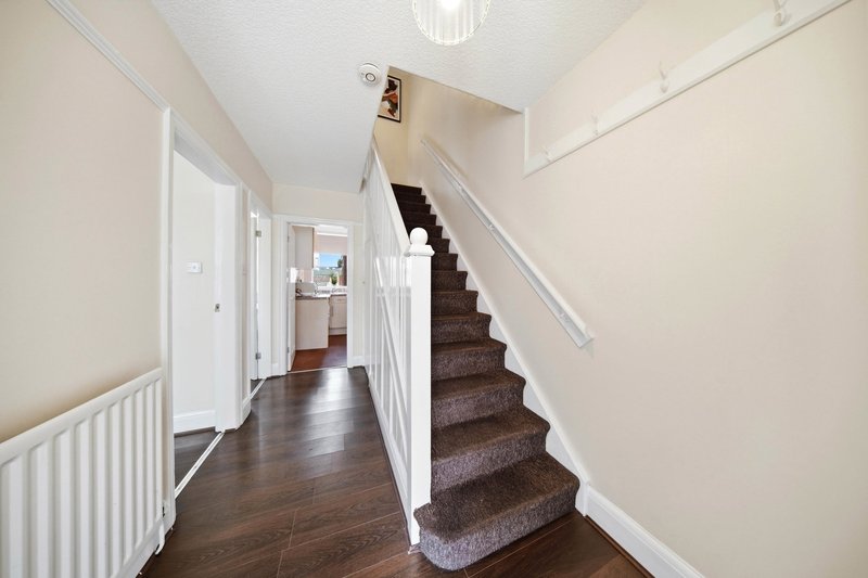 Bright hallway with wooden floor, white radiator, and carpeted staircase with white bannister