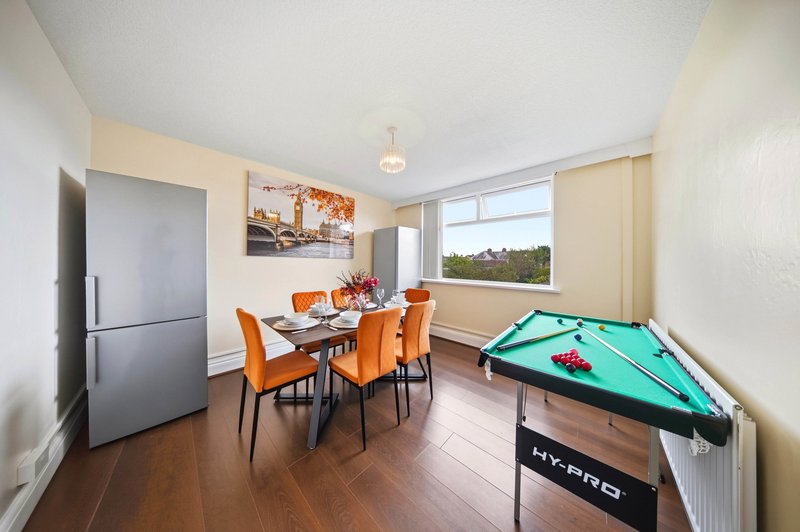Open-plan living space with dining table, orange chairs, pool table, and kitchen area with refrigerator
