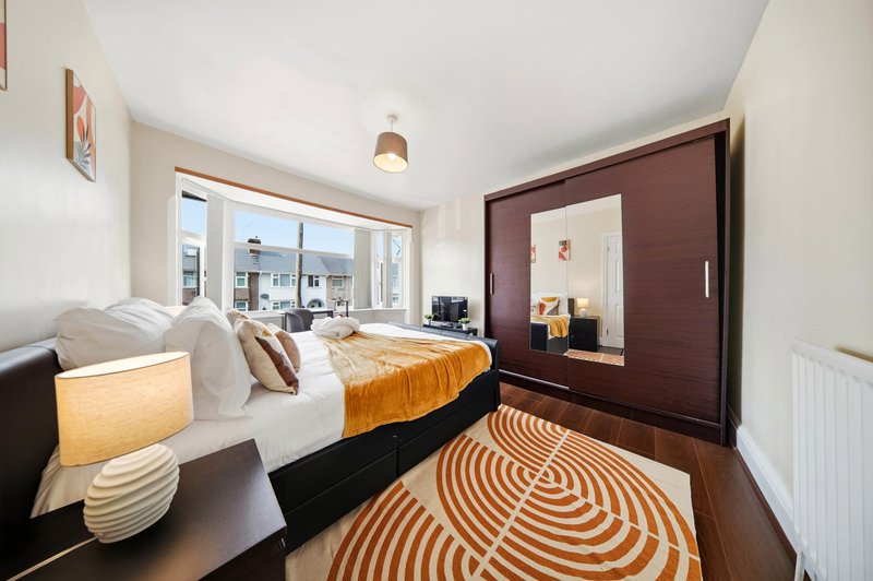 Modern bedroom with double bed, orange throw, patterned rug, and large window with city views