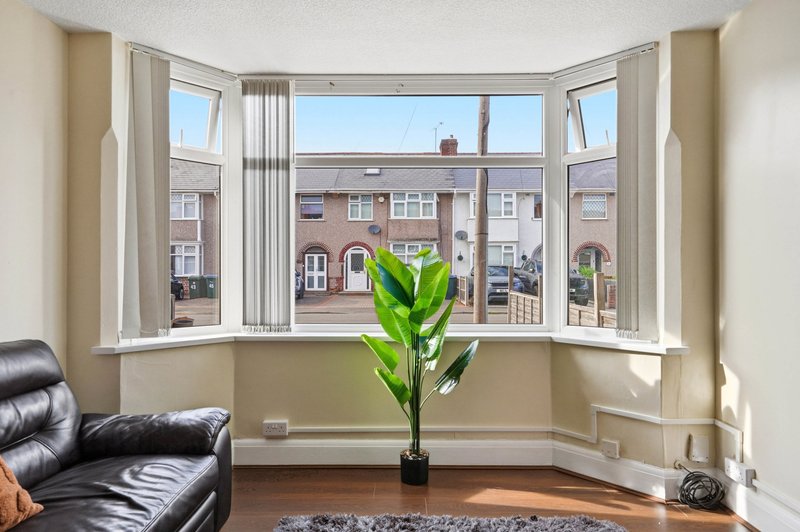 Bay window with view of residential street, potted plant, black leather sofa, wooden floor