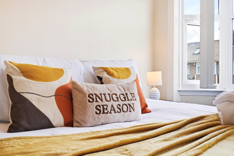 Bright bedroom with white bed, decorative pillows including one with text, wooden headboard and windows