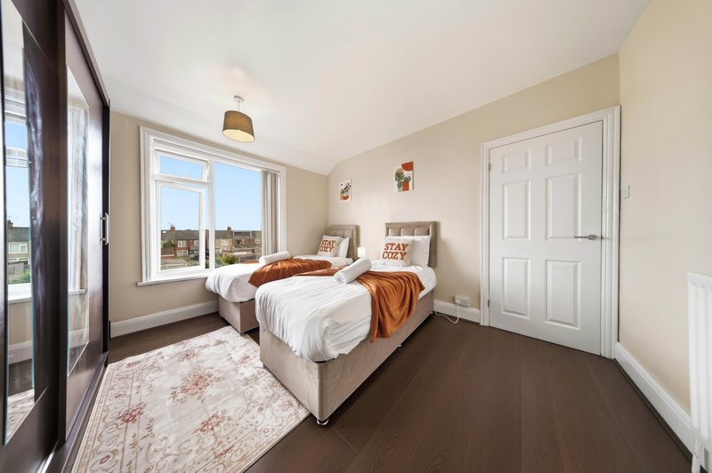 Bright bedroom with twin beds, large windows, dark wood flooring and cream walls