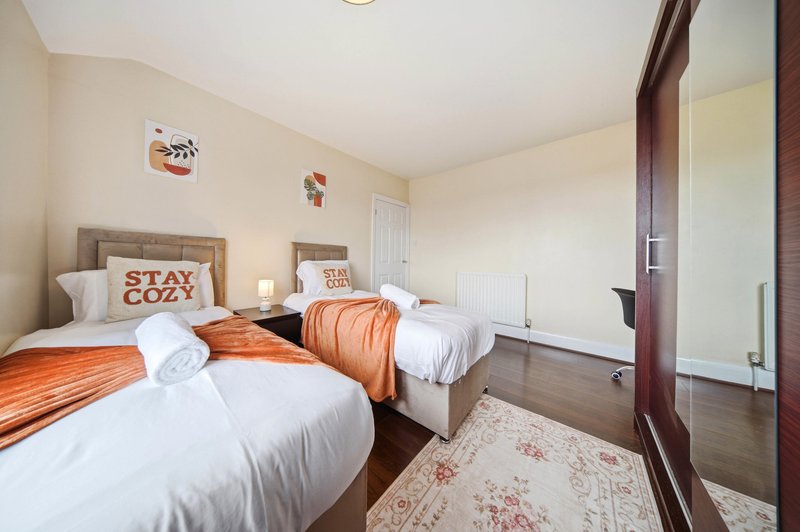 Bright bedroom with two single beds, orange bedding, wooden floor and white walls