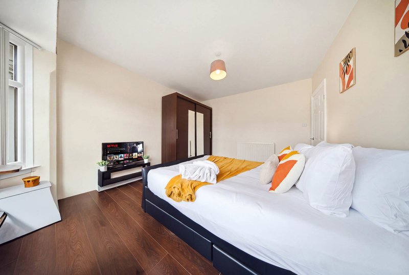 Bright bedroom with double bed, wooden floor, dark wardrobe and window