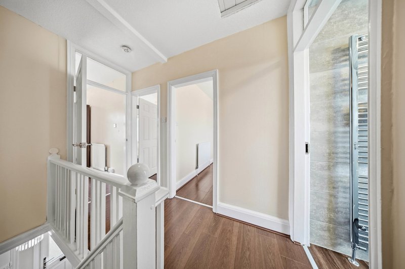 Hallway with wooden flooring, cream walls, white doors and staircase railing