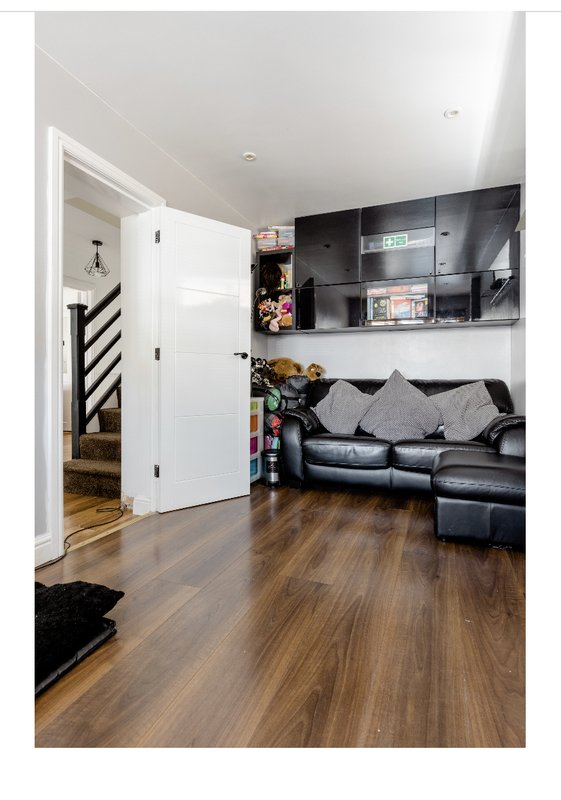 Open-plan living room with black leather sofa, wall-mounted TV, wooden flooring and white door