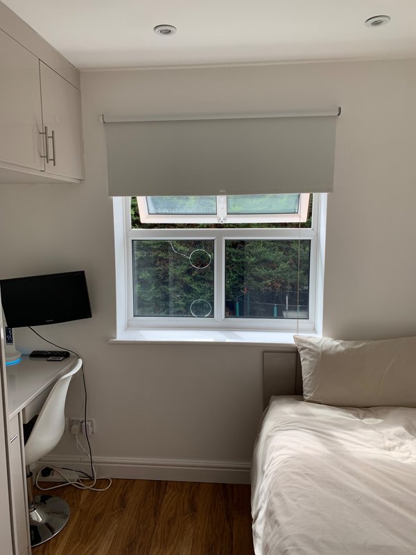 Small bedroom with single bed, desk with monitor, window with roller blind and wooden floor
