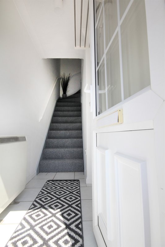 Staircase with dark grey carpet, geometric patterned floor mat, white walls and bannister
