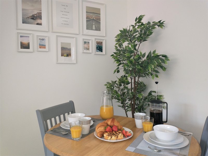 Dining table set for breakfast with fruit, juice and tableware, potted plant behind