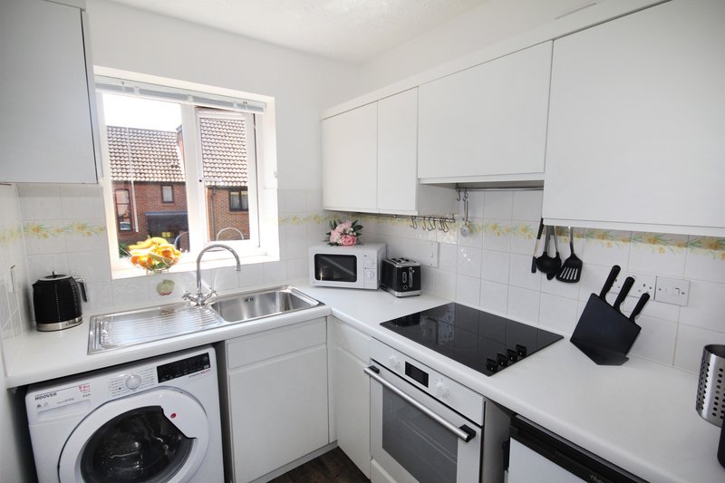 Modern white kitchen with sink, cooktop, washing machine and window overlooking garden