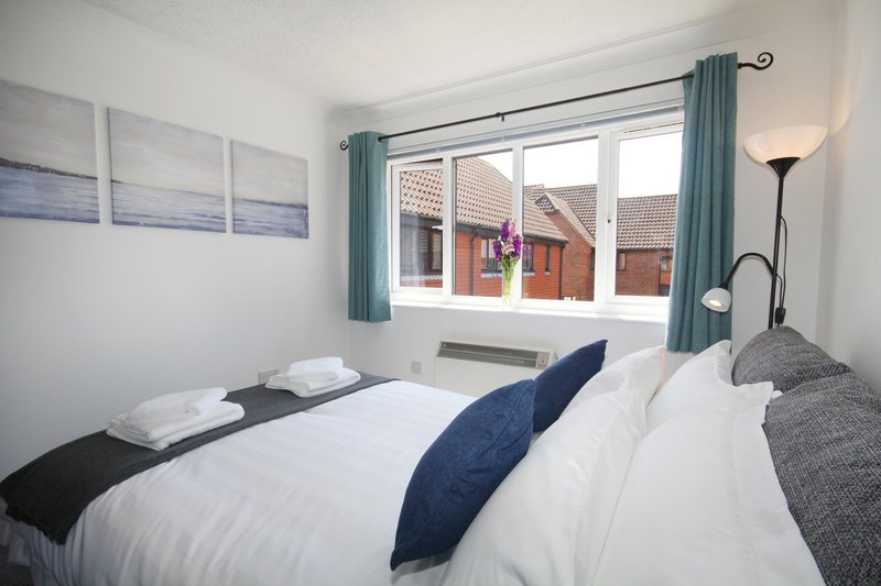 Bright bedroom with double bed, white bedding, teal curtains and street view
