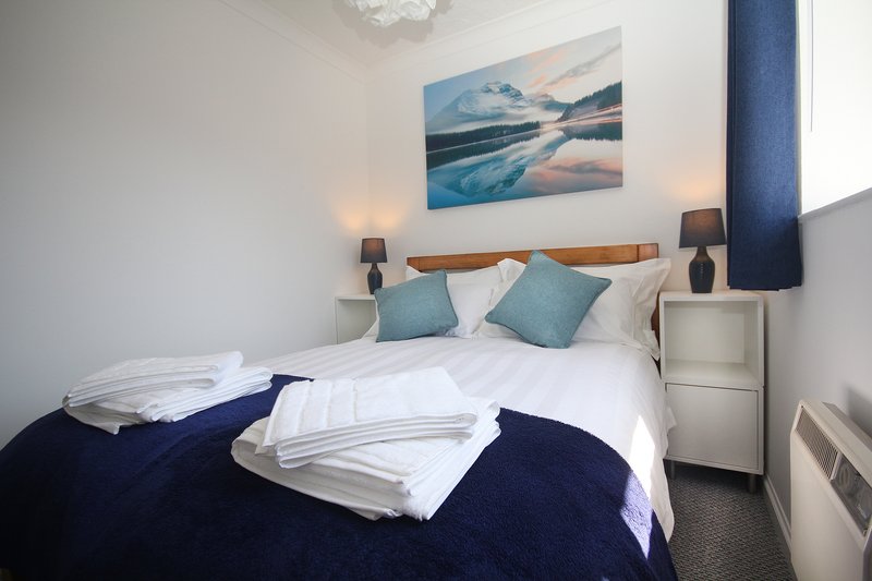 Bright bedroom with double bed, white bedding, blue cushions and wall art above headboard