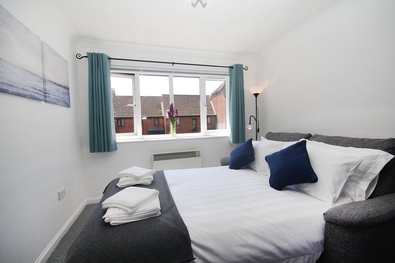 Bright bedroom with double bed, white bedding, navy cushions, teal curtains and window view