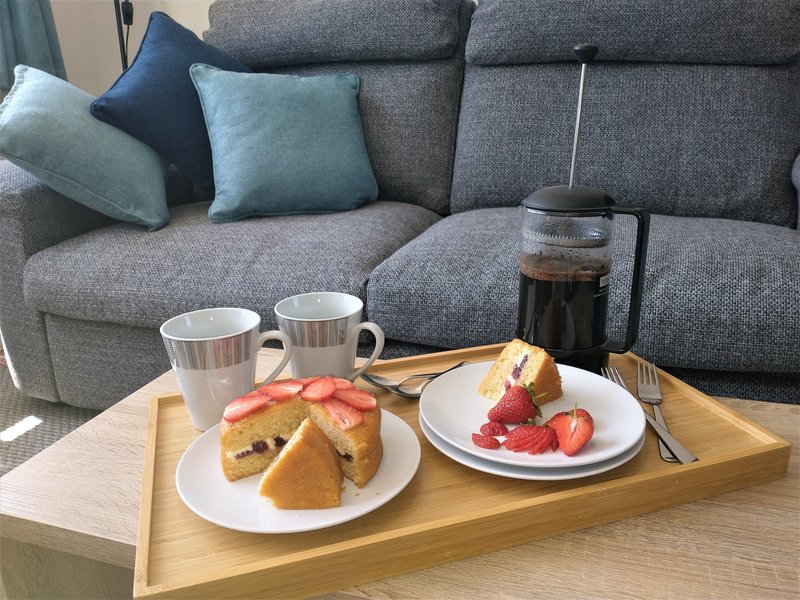 Living room with grey sofa, cushions, and wooden table set with breakfast items
