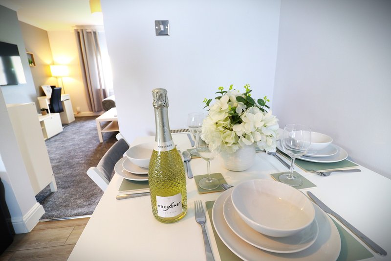 Dining table set for dinner with prosecco bottle, flowers, place settings and view into living area