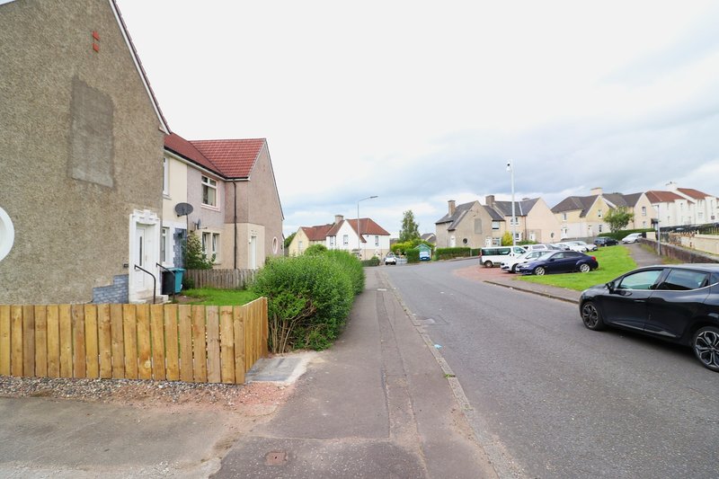 Street view of stone residential houses with wooden fence, parked cars and suburban neighborhood