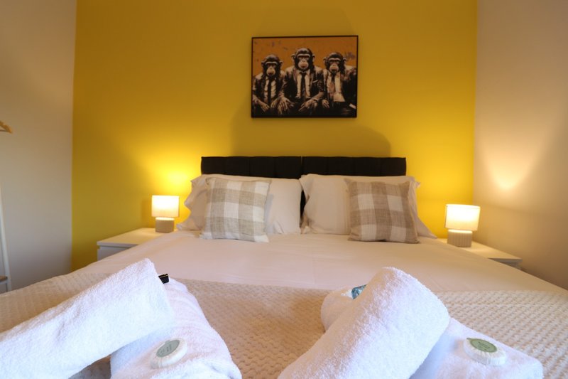 Bright yellow bedroom with double bed, white bedding, and framed wall art above headboard