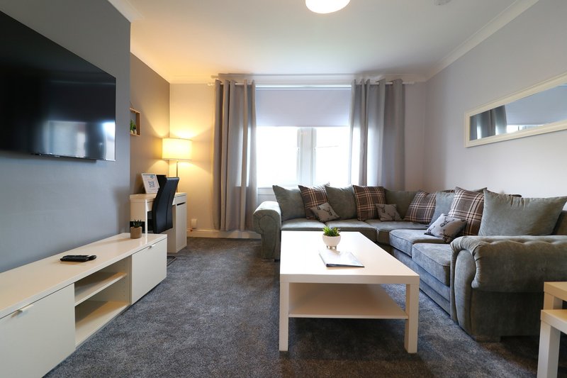 Modern living room with grey sofa, white coffee table, TV unit and window with curtains