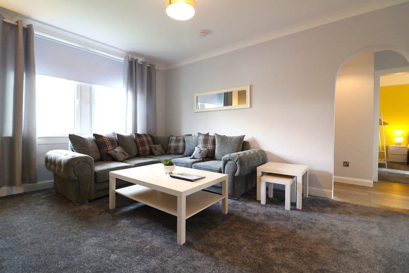 Modern living room with grey corner sofa, wooden coffee table, and large windows with curtains