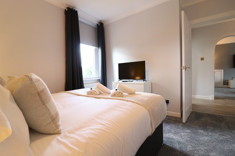 Modern bedroom with double bed, cream bedding, decorative pillows, wall-mounted TV and window with black curtains