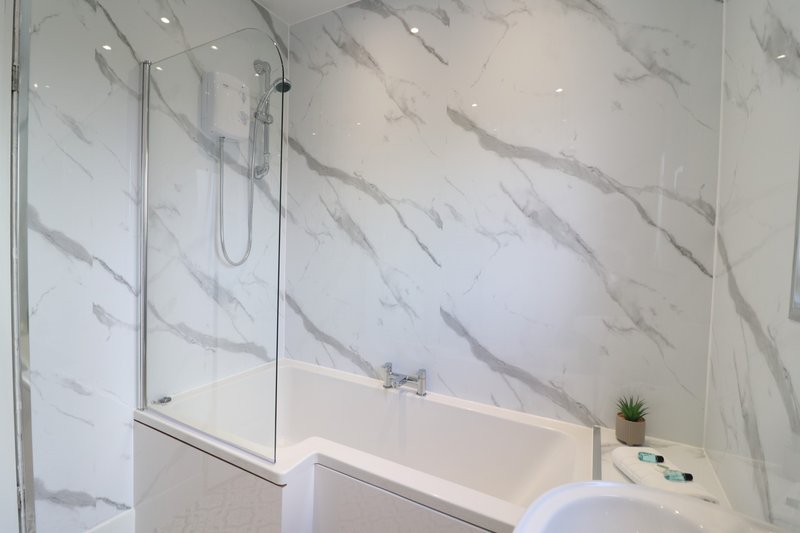 Modern bathroom with marble-effect tiles, white bathtub, glass shower screen and recessed lighting