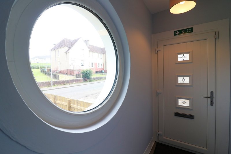 Interior hallway with porthole window overlooking residential street and modern door
