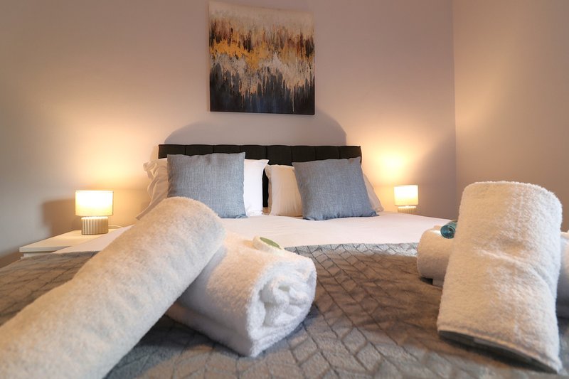 Modern bedroom with double bed, rolled towels, bedside lamps and abstract wall art