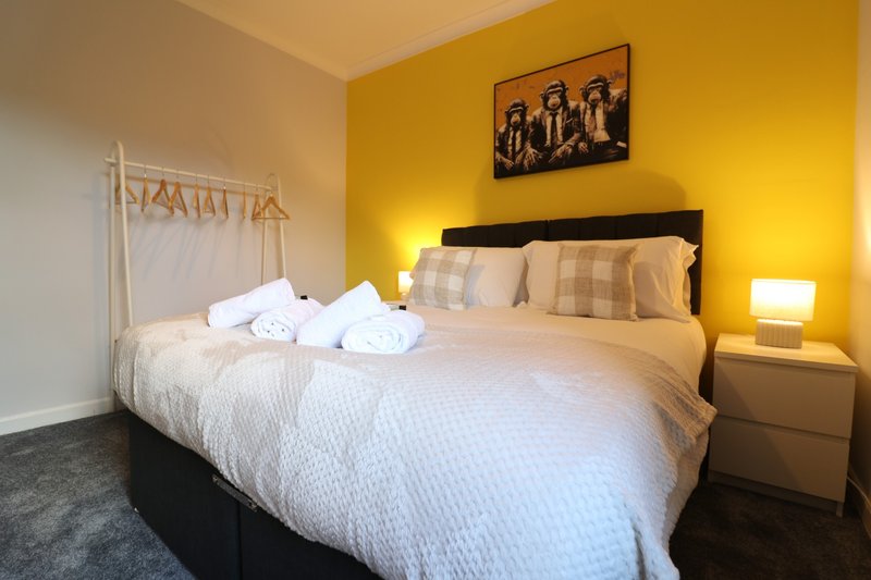 Bright bedroom with double bed, yellow accent wall, bedside lamp and framed artwork