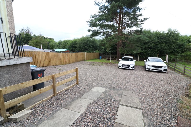 Gravel driveway with parking area, wooden fencing, landscaping and trees