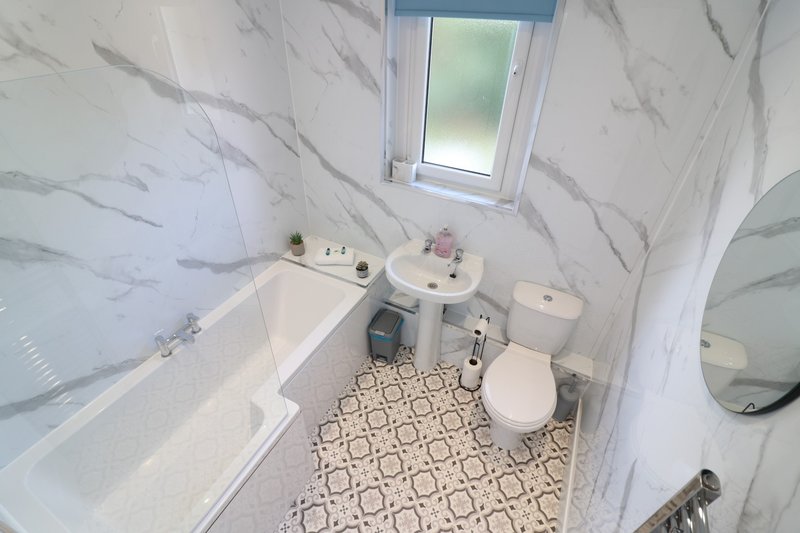 Clean bathroom with white marble walls, bathtub, pedestal sink, toilet, and patterned floor tile