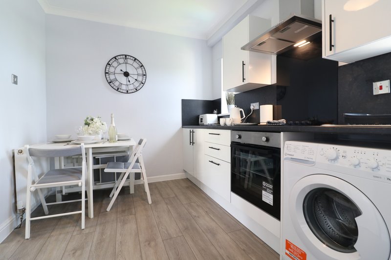 Modern kitchen with white dining table, black countertop, built-in oven and washing machine