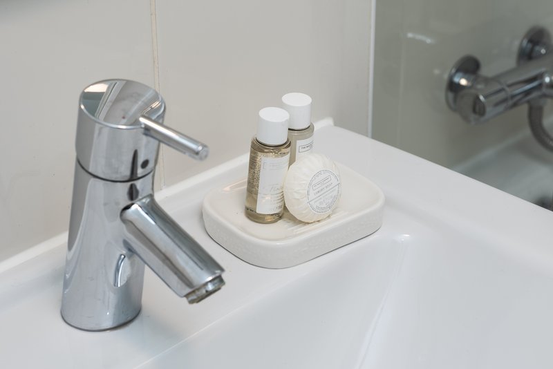 Modern bathroom sink with chrome faucet and white countertop with toiletries and soap dispenser