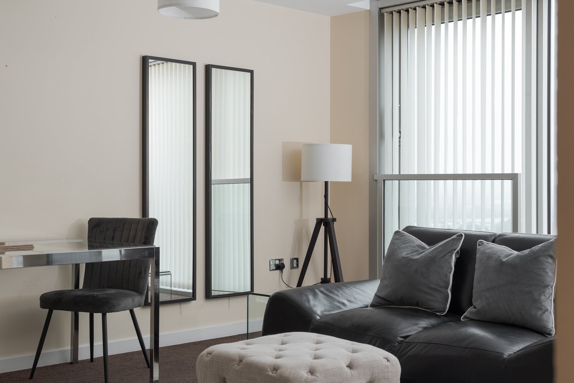 Modern studio apartment with black leather sofa, desk chair, tripod lamp and vertical blinds