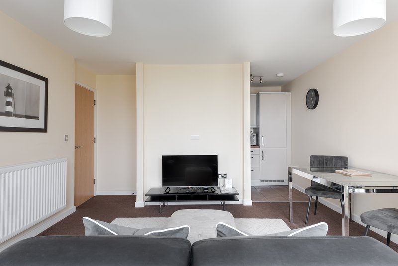 Open-plan living space with grey sofa, TV, dining area and kitchen visible