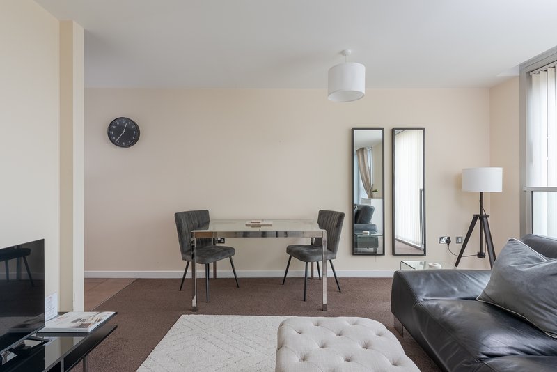 Modern open-plan living space with dining table, black chairs, sofa, and wall clock