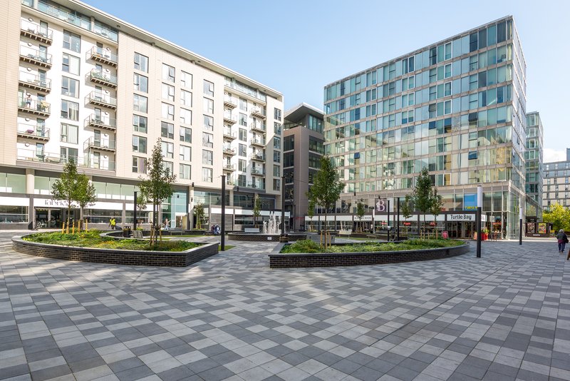 Modern apartment building complex with paved plaza, landscaping, and surrounding residential towers