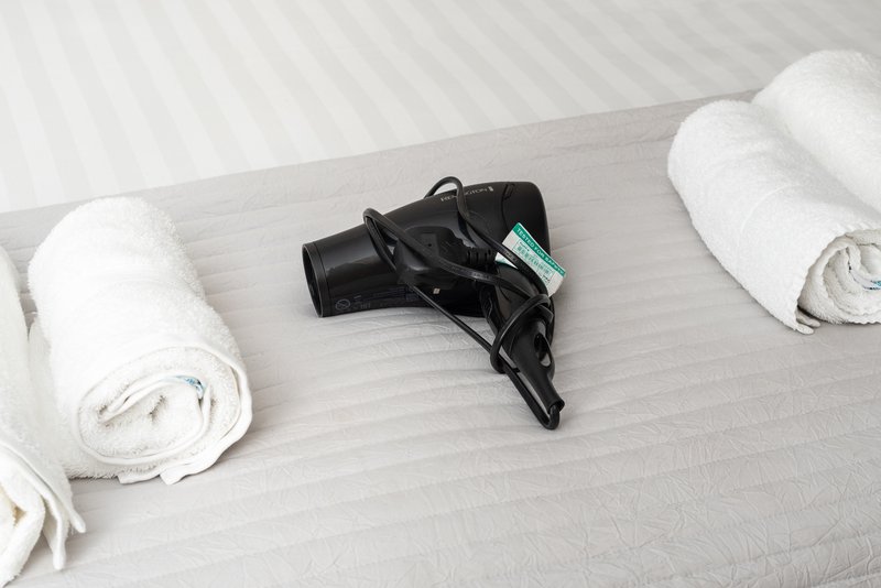 Bed with white rolled towels and black hair dryer placed on white bedding