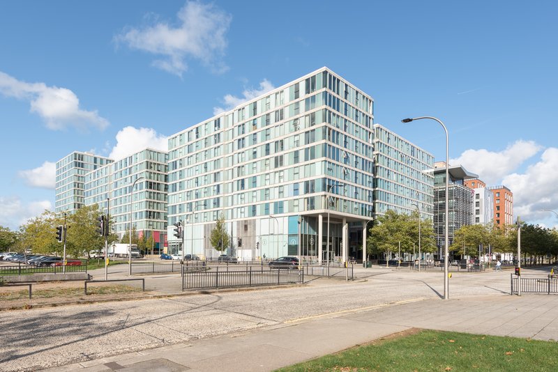 Modern multi-story residential building with glass and white facade, plaza and trees
