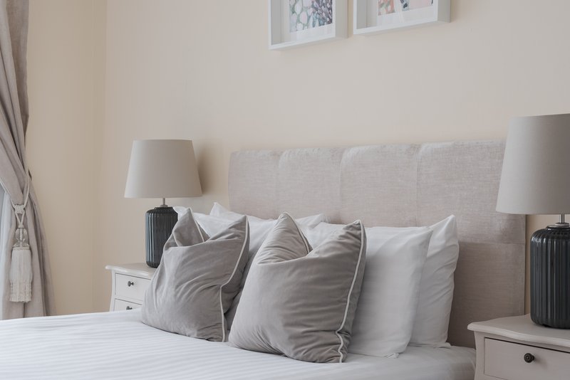 Bedroom with upholstered headboard, decorative pillows, white bedding and matching bedside lamps