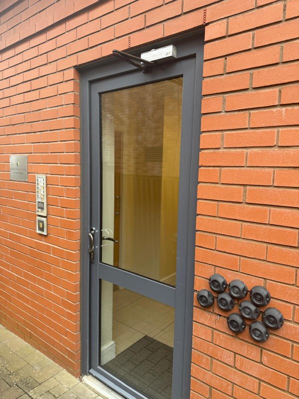 Red brick building exterior with gray framed door and number plaques