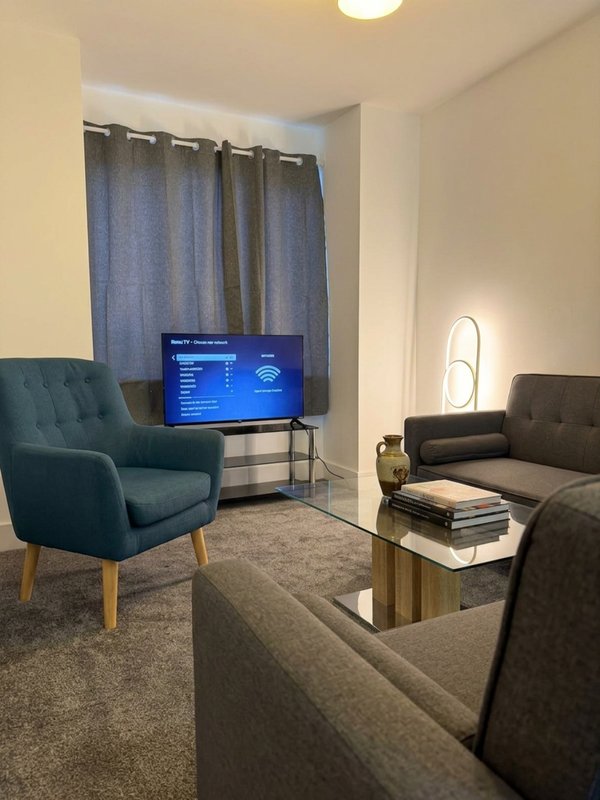 Living room with teal armchair, sofa, TV on stand, coffee table and blue curtains