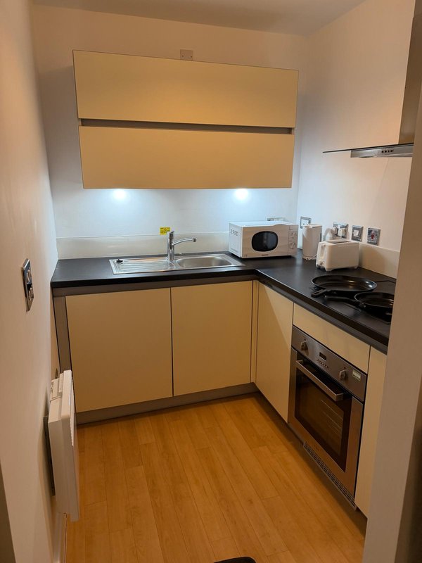 Small modern kitchen with yellow cabinetry, black countertop, built-in oven and wooden flooring