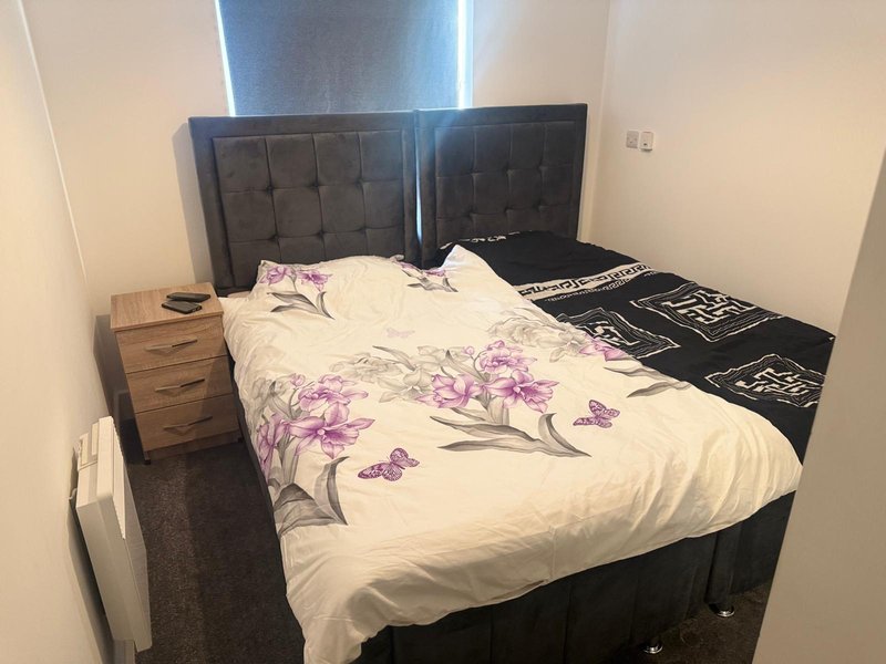 Bedroom with double bed, black padded headboard, floral duvet, and wooden nightstand
