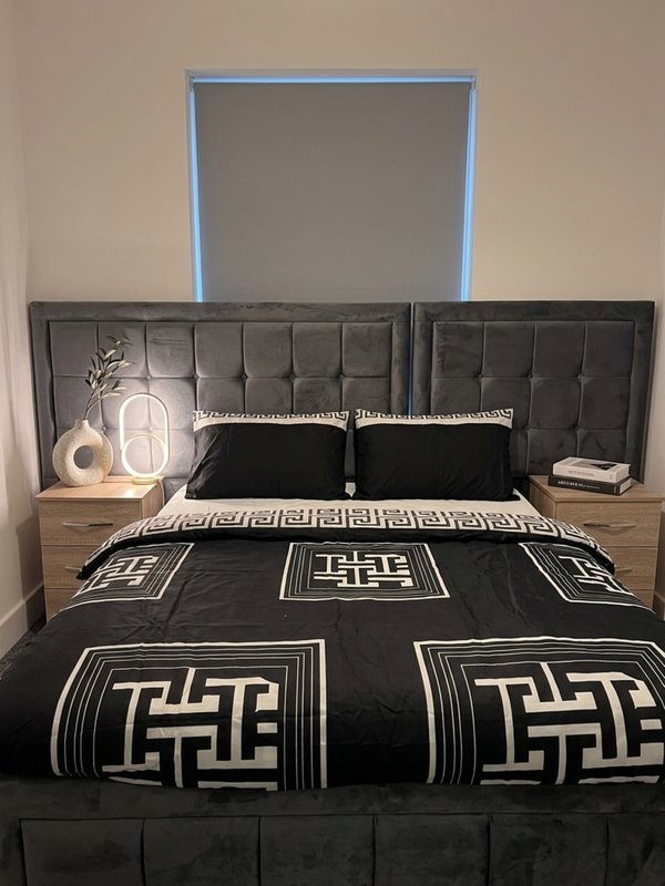 Modern bedroom with black upholstered headboard, geometric patterned bedding, neon-lit wall art, and wooden nightstands