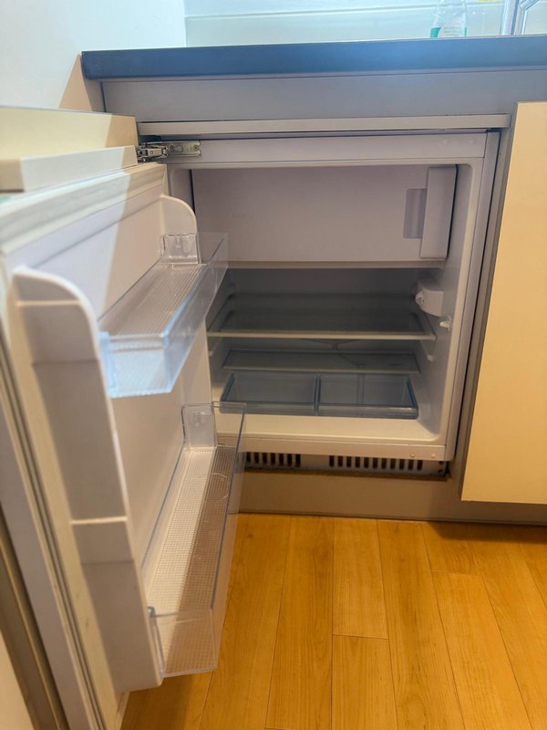 Open refrigerator with empty shelves and wooden floor visible below