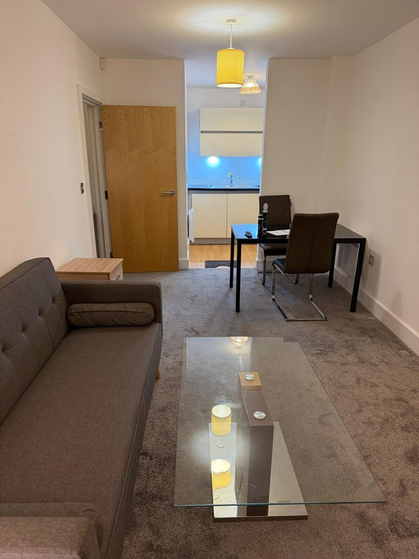 Open-plan living area with grey sofa, glass coffee table, desk setup, and yellow pendant light